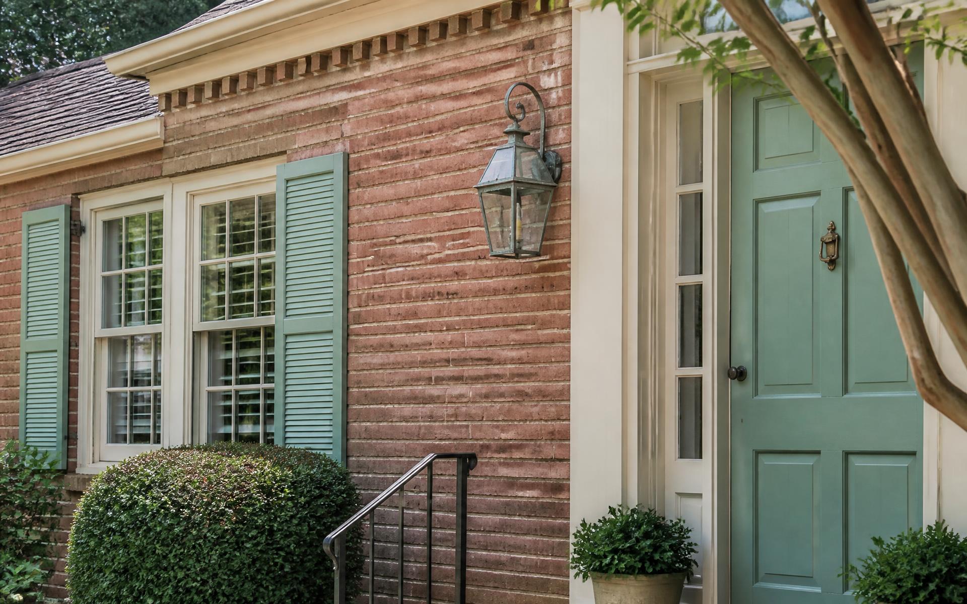 A mid-century brick ranch home with black steel windows and boxwood hedges